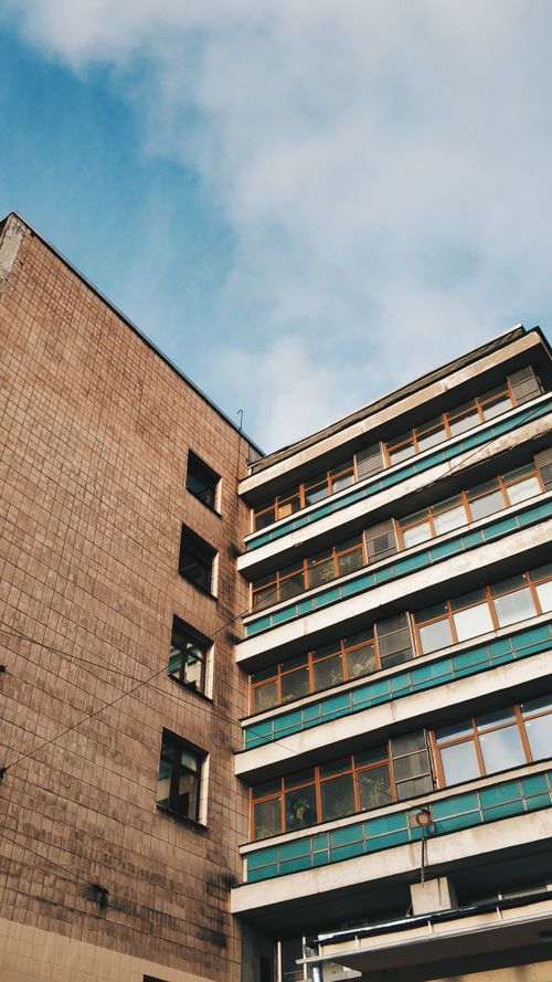 Free From below facade of low cost brick condominium with long weathered balconies against blue sky Stock Photo