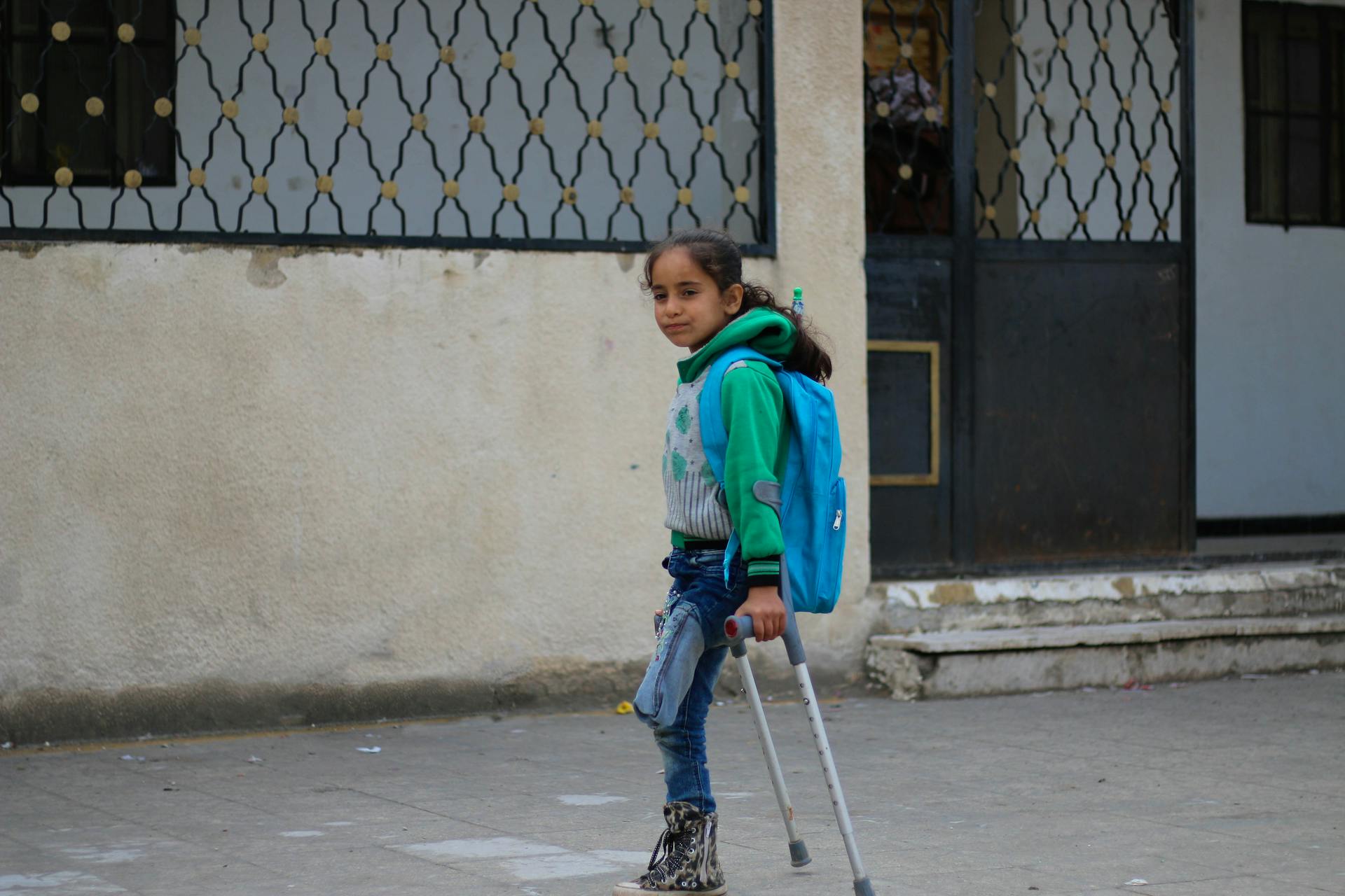 A young girl with a backpack using crutches on a street in Idlib, Syria. Bright and hopeful.