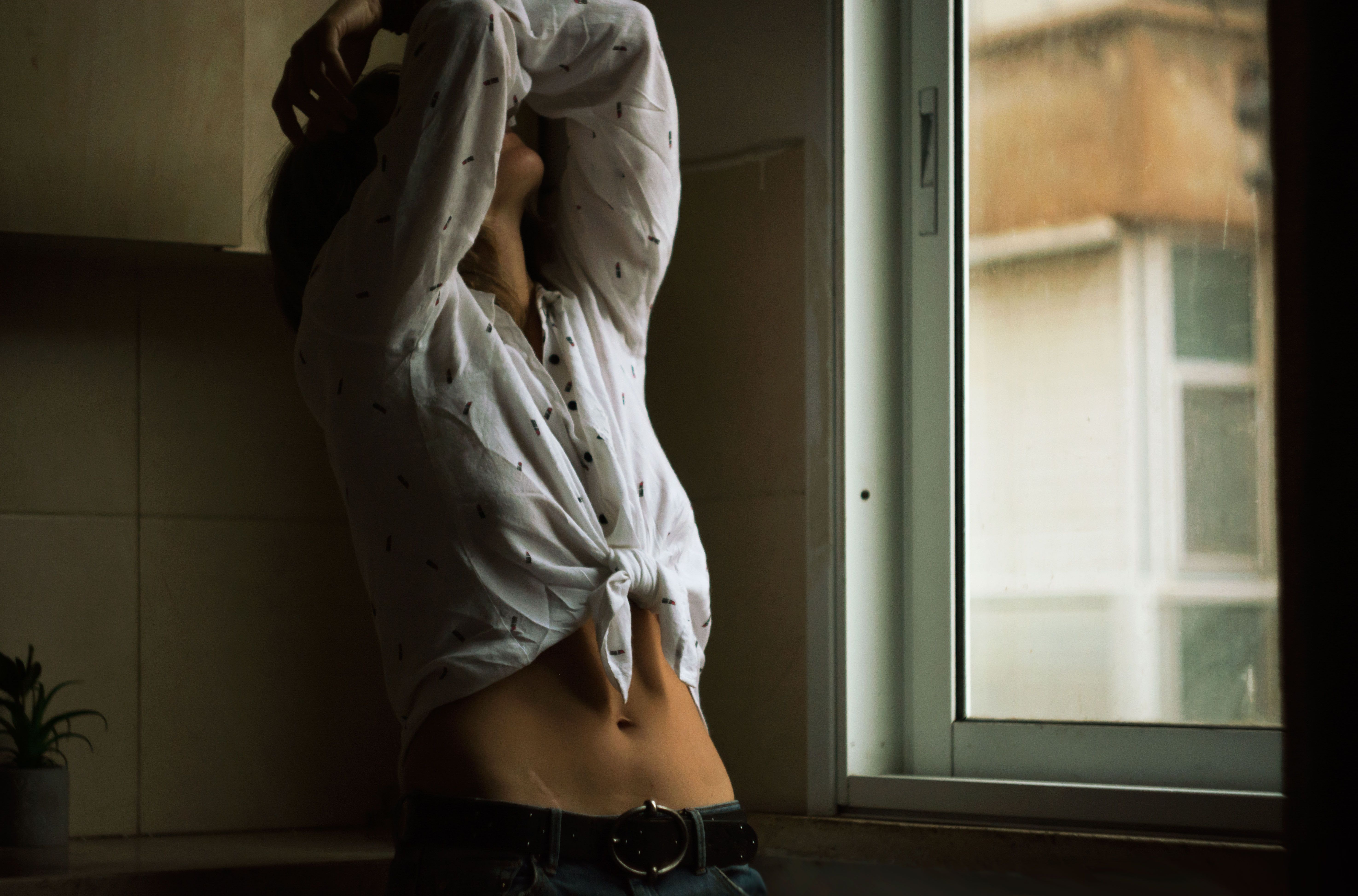 Woman posing with arms raised in a bright kitchen near window.