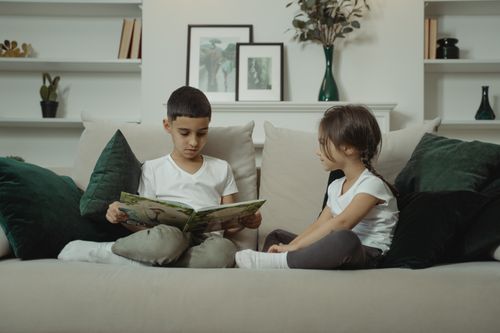 Free A boy and girl sit on a sofa engrossed in a book, creating a warm and homely atmosphere. Stock Photo