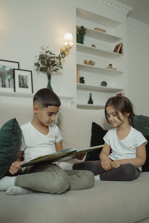 Free Two young children enjoying a book on a comfortable sofa, indoor setting. Stock Photo