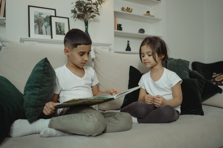 A Boy And A Girl Reading A Book On The Couch