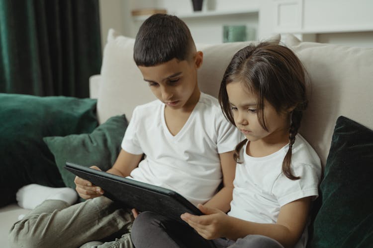 Siblings Sitting On The Sofa Sharing A Tablet Computer 