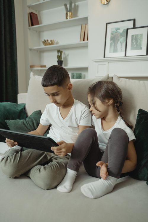 Free Two young children enjoying a tablet sitting on a sofa in a cozy living room setting. Stock Photo