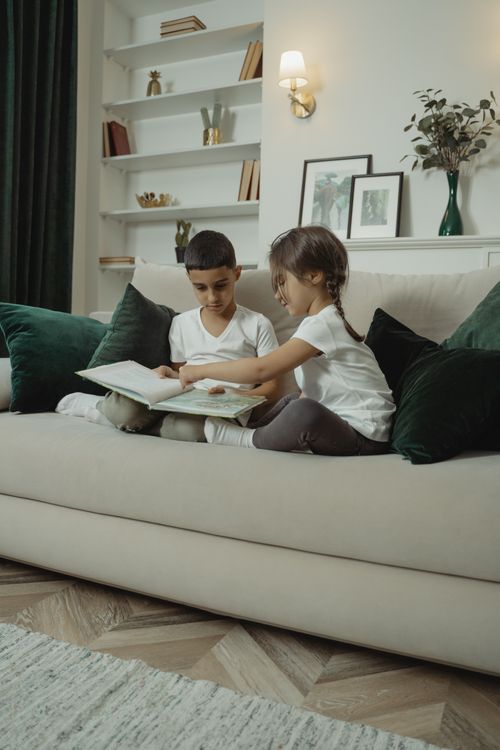 Free Young siblings engaged in reading on a sofa, showcasing comfort and togetherness in a home setting. Stock Photo