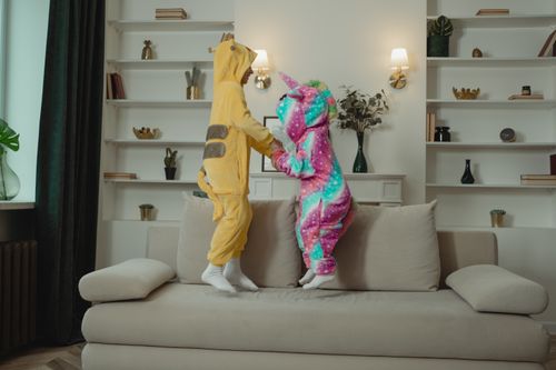 Free Two children in colorful animal costumes having fun jumping on a sofa indoors. Stock Photo
