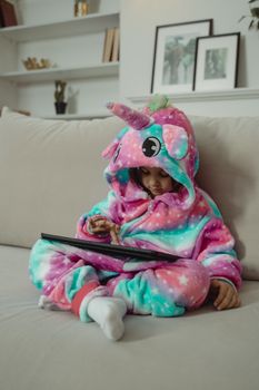 一个可爱的年轻女孩穿着独角兽服装，坐在室内的沙发上专注地看着平板电脑