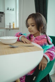 Adorable girl in starry pajamas sitting at a breakfast table indoors.