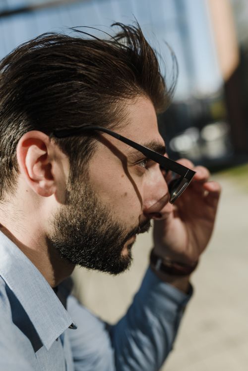 Free Close-up side profile of a man with beard and glasses adjusting frames outdoors during the day. Stock Photo