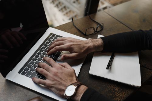 Free Focused view of hands typing on a laptop keyboard with a notepad and pen nearby on a desk. Stock Photo