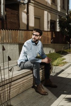 一个戴眼镜的男人若有所思地坐在户外阳光下的长凳上