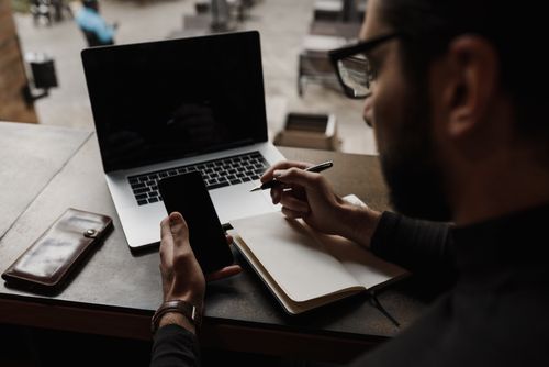 Free Businessman multitasking with smartphone and notebook at a café table. Stock Photo