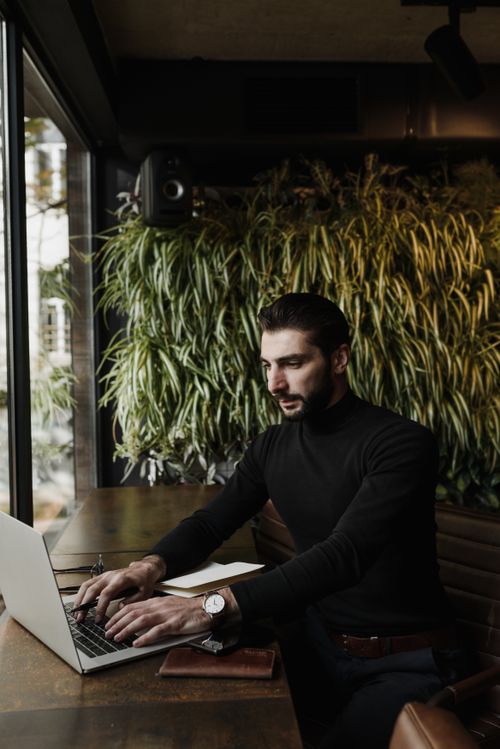 Free Young man in a black sweater working on a laptop in a modern cafe with green decor. Stock Photo