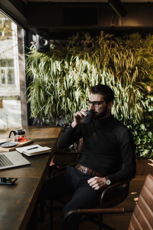 Free A fashionable man in a black turtleneck sitting in a cafe with coffee and a laptop. Stock Photo