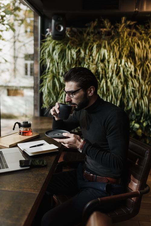 Free Man sipping tea by a laptop in a stylish office with a vertical garden. Stock Photo