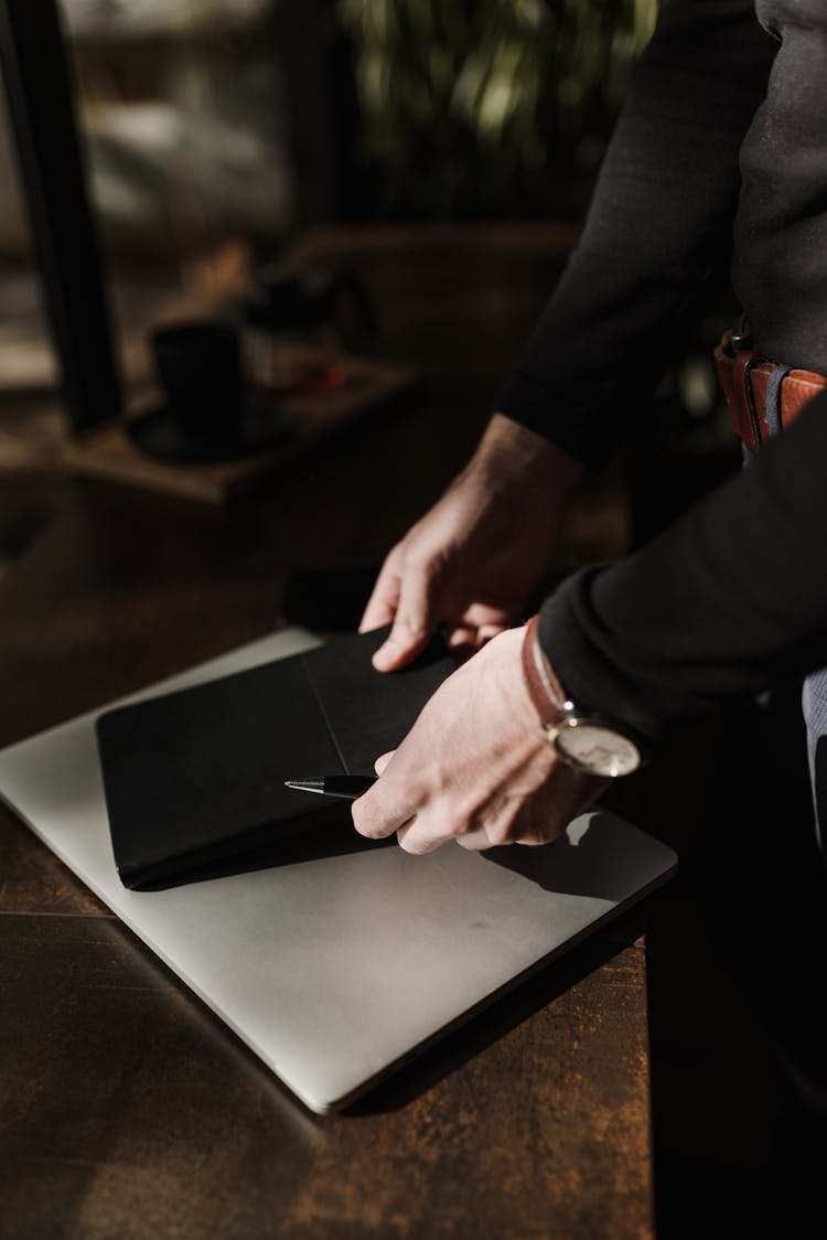 A Person Putting The Black Notebook On Top Of A Laptop