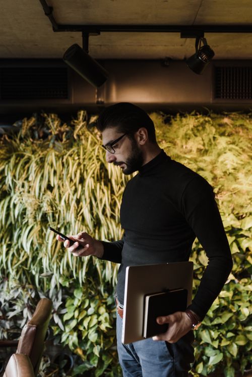 Free Confident businessman holding notebook and smartphone in a stylish office with vertical garden. Stock Photo