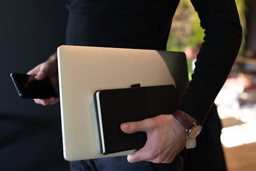 A person carrying a laptop, smartphone, and notebook, indoors.