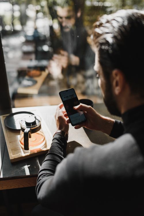 Free Person holding a phone in a cafe, reflecting modern lifestyle. Stock Photo