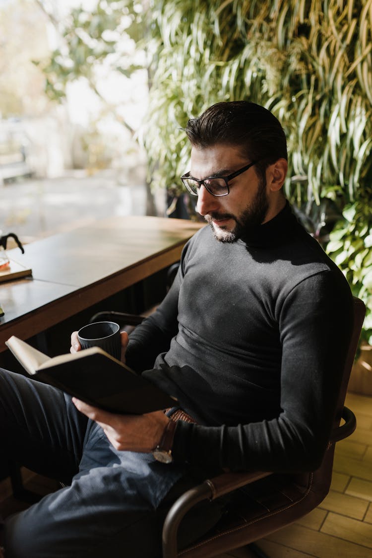 Man Sitting On Chair Reading Book