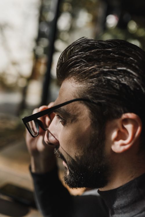Free Close-up side view of a bearded man outdoors adjusting glasses in natural daylight. Stock Photo