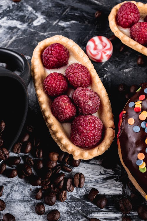 Free High angle sweet appetizing raspberry tartlet placed on table near delicious pastries and scattered fragrant coffee beans Stock Photo