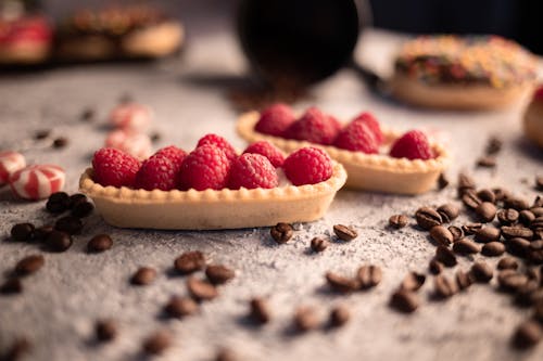 Free Delicious fresh raspberry tartlets placed on table amidst aromatic coffee beans and sweets Stock Photo