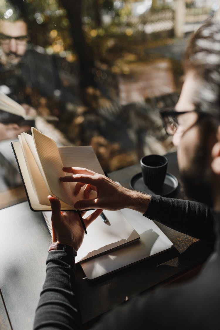 Man In Black Long Sleeve Shirt Looking Through Pages Of A Notebook