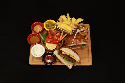 Top view of a gourmet burger meal with sides, sauces, and fries on a wooden board.