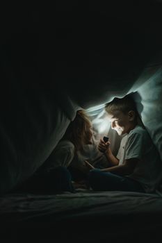 两个孩子拿着手电筒在毯子堡垒里享受玩耍的时刻