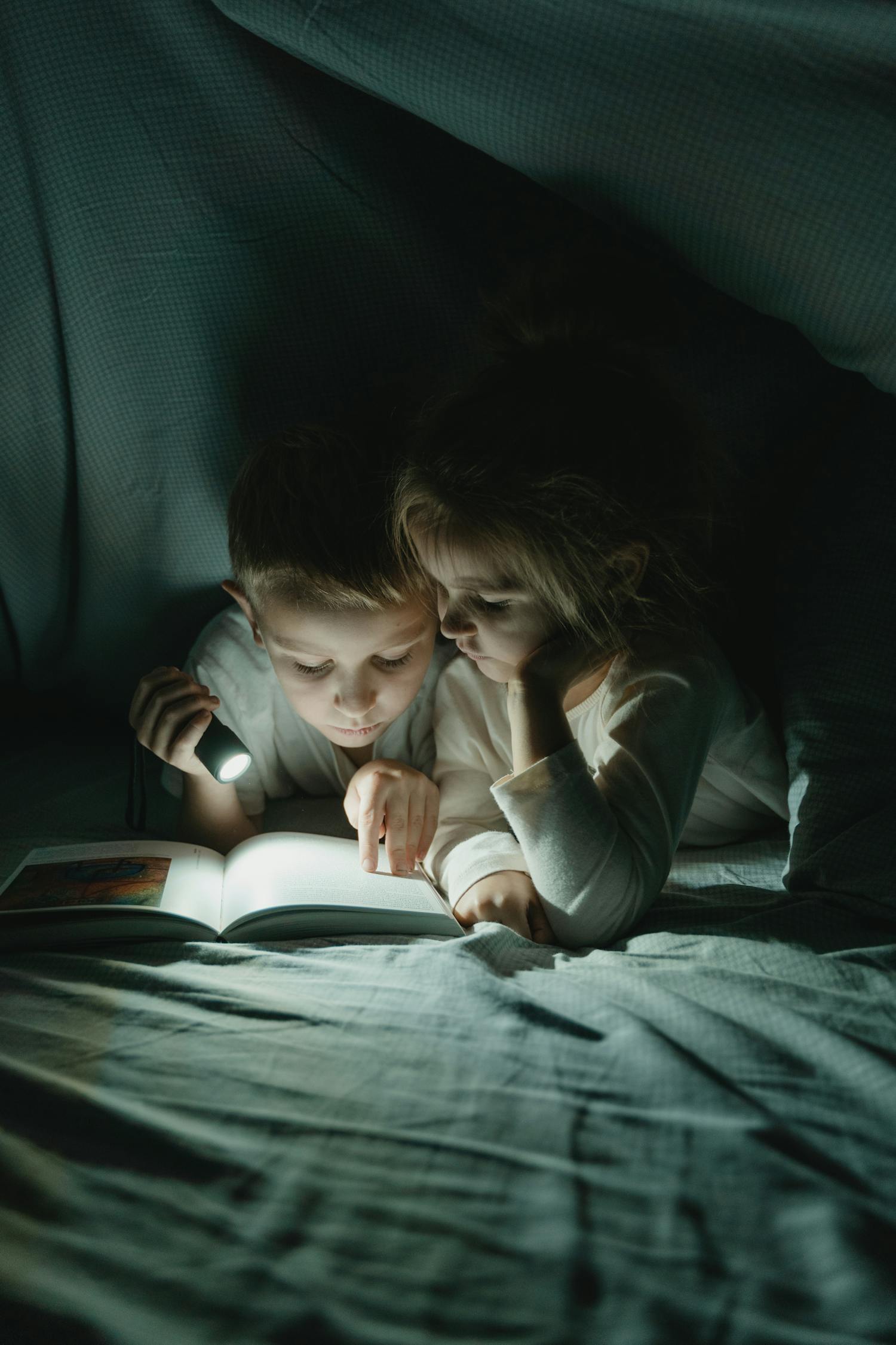 Girl and Boy Reading Book Under Blanket