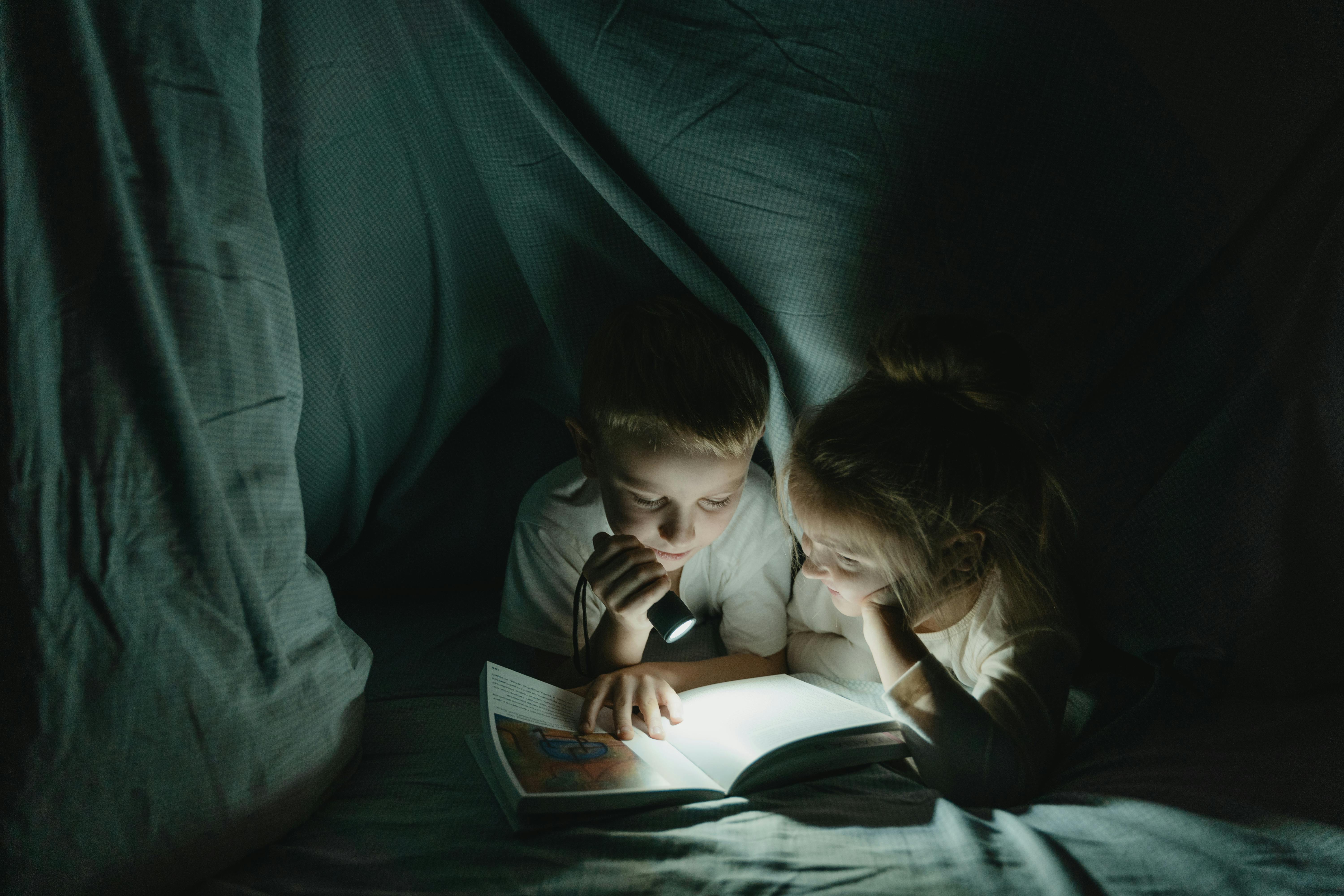 girl and boy reading book in blanket fort