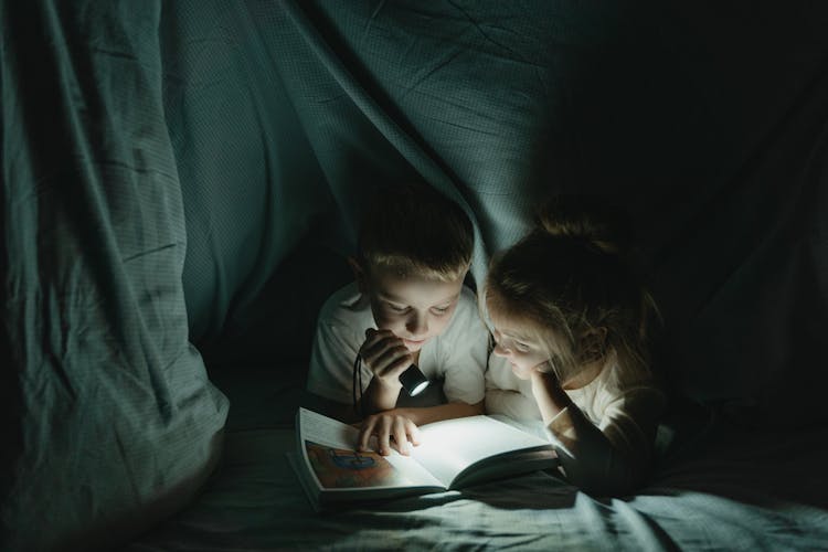 Girl And Boy Reading Book In Blanket Fort