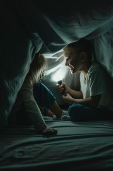 晚上，两个孩子拿着手电筒，在舒适的毯子堡垒里讲故事