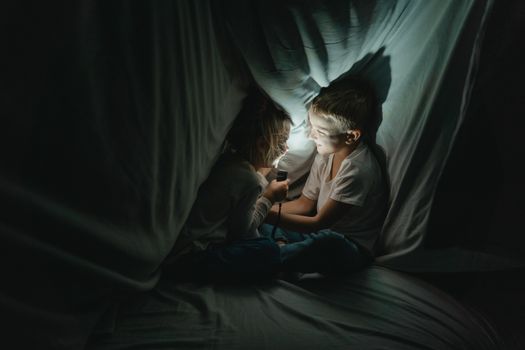 两个孩子喜欢在毯子堡垒里，借着手电筒的光讲故事