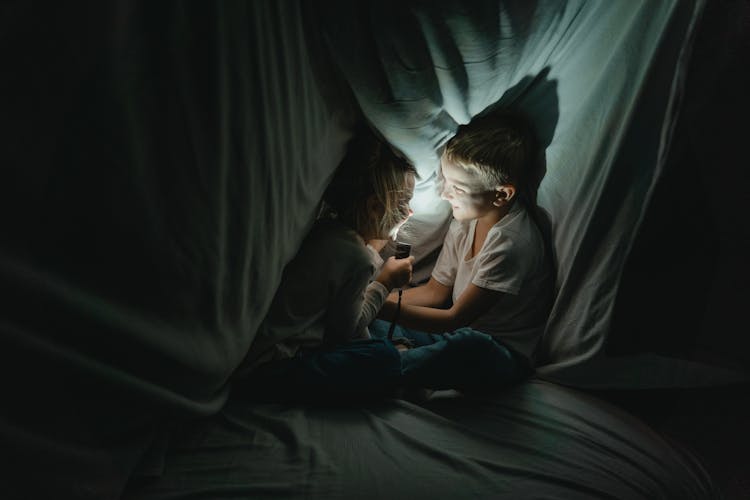 Girl And Boy Telling Stories In Blanket Fort