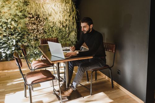 Free Adult man working on a laptop in a stylish indoor workspace with a green wall background. Stock Photo