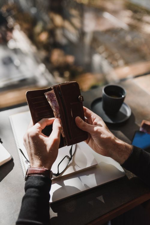 Free Person holding a wallet with currency, next to a cup of coffee on a table. Stock Photo