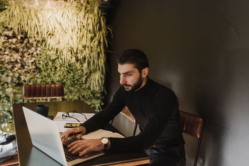 Free Businessman working on laptop in a stylish indoors office with greenery wall and sleek furniture. Stock Photo