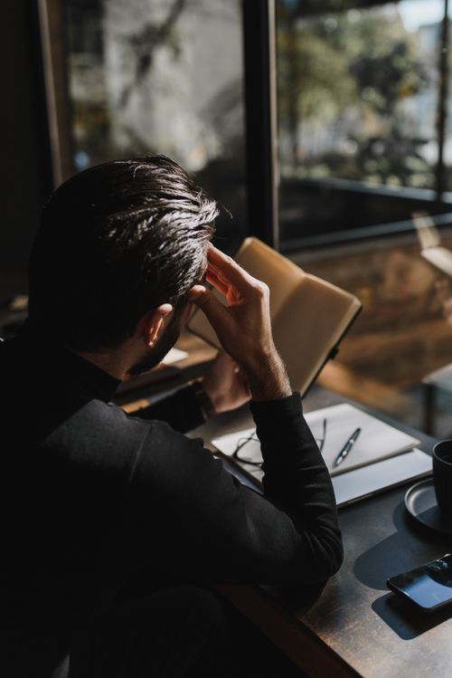 Free Rear view of a man reading by a sunlit window in a cozy cafe, creating a reflective mood. Stock Photo