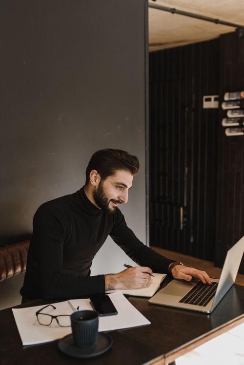 Free Man in black sweater focused on laptop work in a stylish cafe environment. Stock Photo