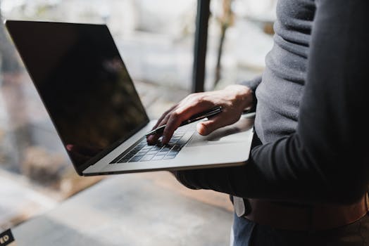 A close-up image of a man using a laptop in a bright, modern office setting.