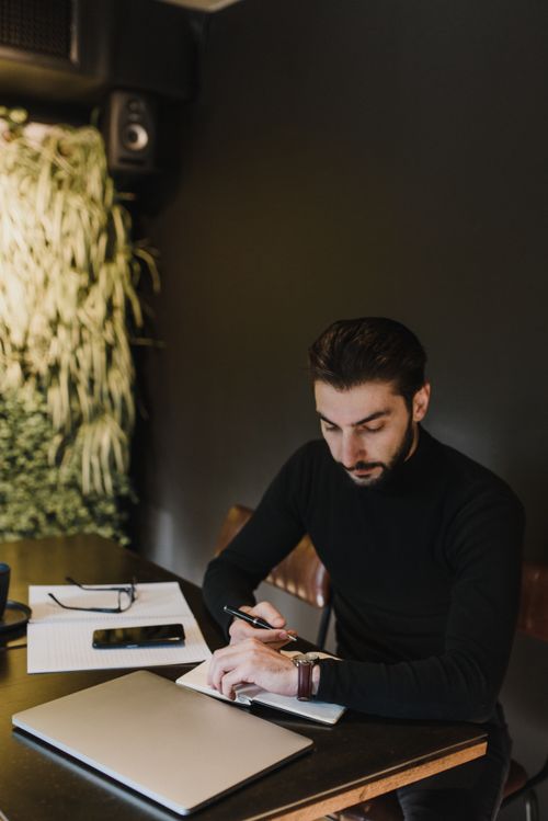 Free Man working at a table with laptop, notebook, and smartphone in a stylish office environment. Stock Photo