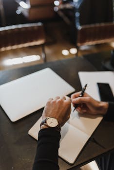 A top view of hands writing in a notebook at a modern workspace with a laptop.