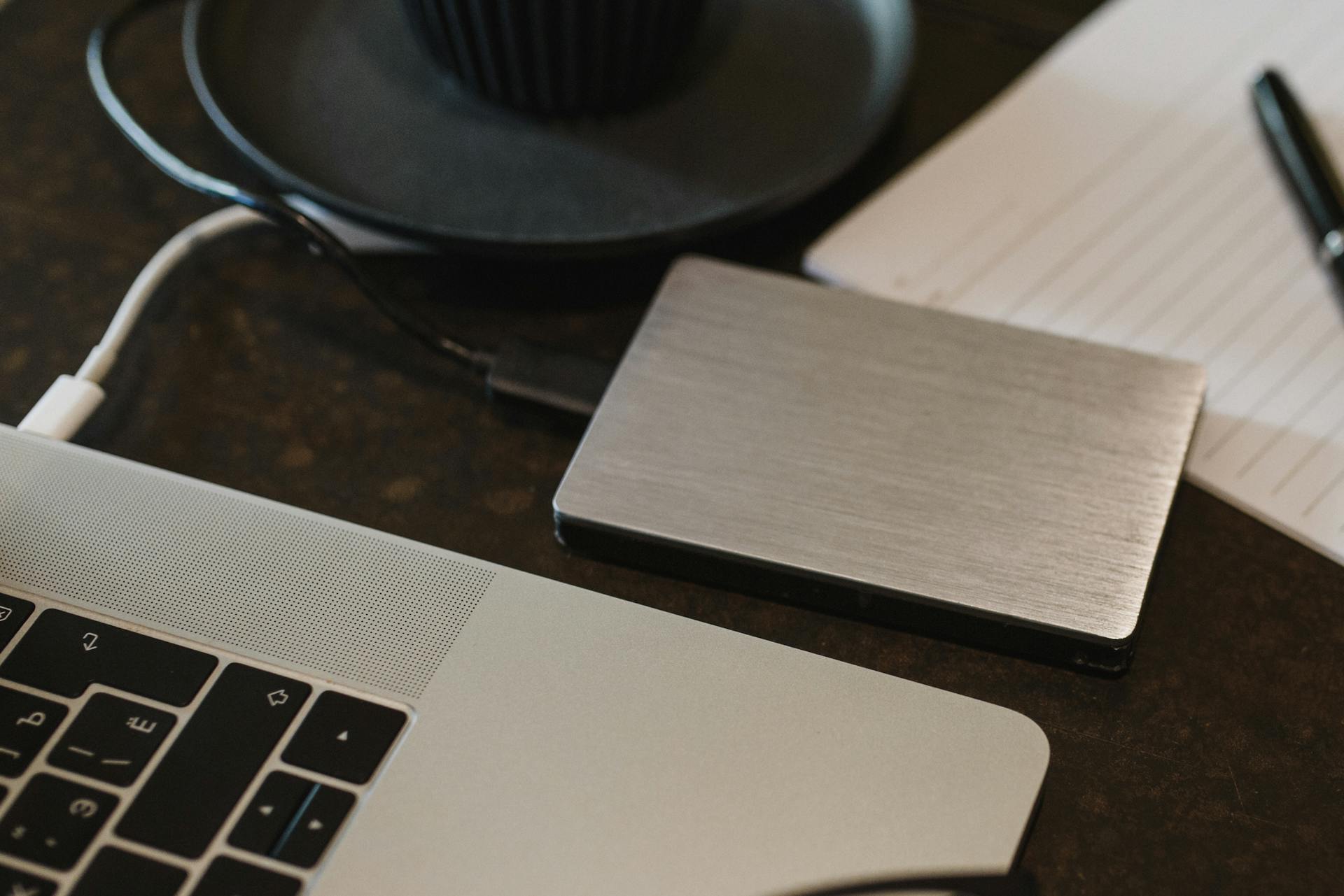 Closeup of an external hard drive connected to a laptop with a USB cable on a desk.