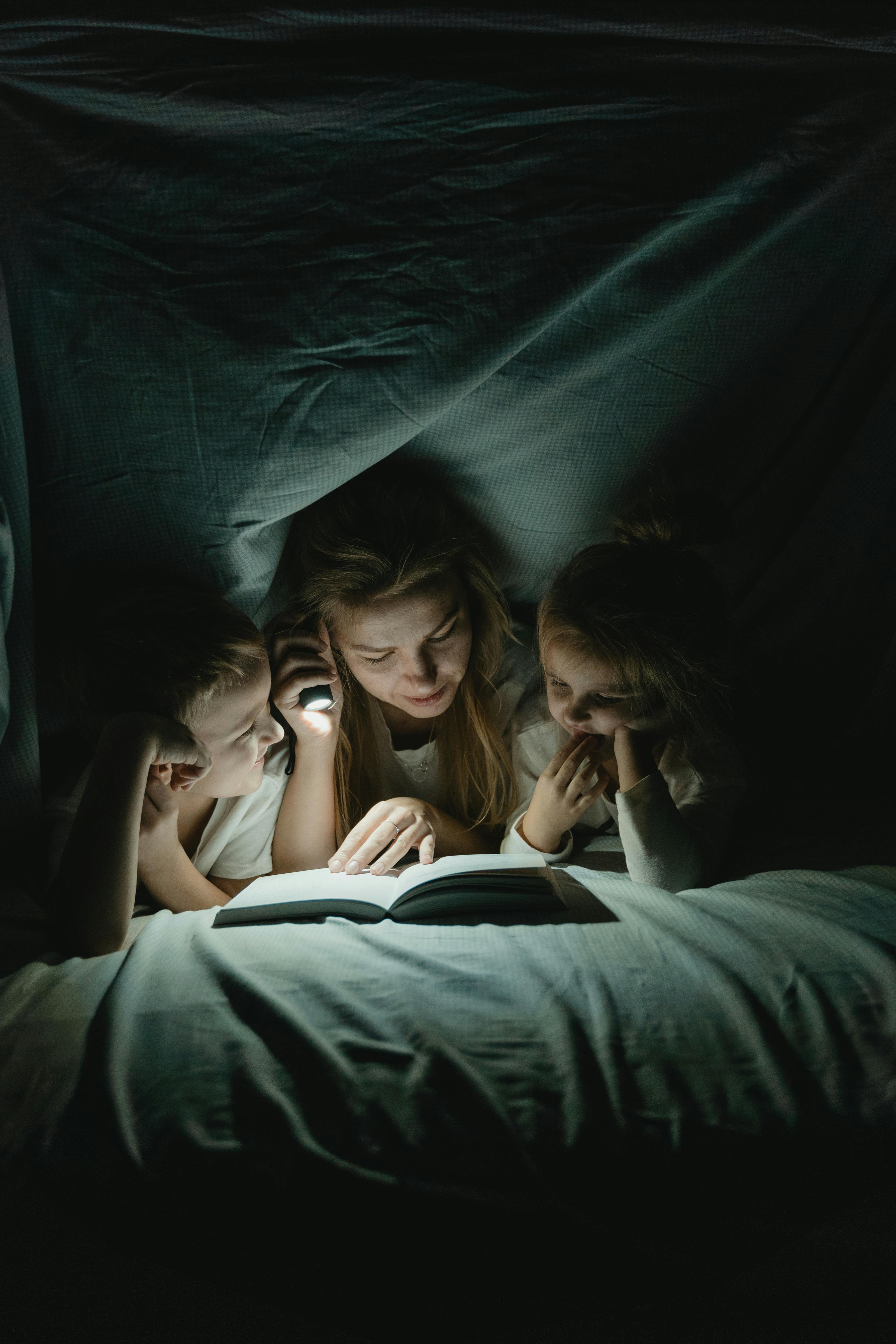 a woman reading a book to her children under a blanket