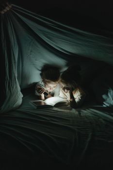 晚上，两个孩子打着手电筒，在毯子下看书，营造出舒适的氛围