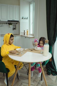 Two children in pajamas having breakfast with cereal and milk in a cozy kitchen.