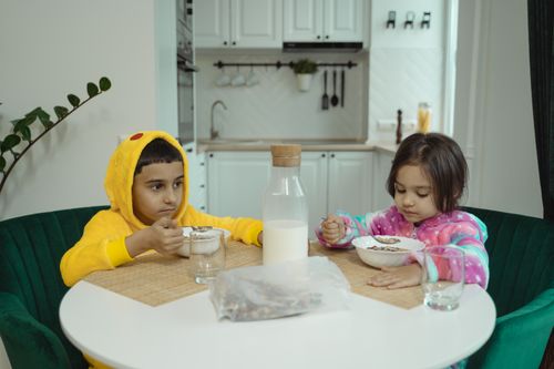 Free Two adorable siblings in cozy pajamas enjoying breakfast cereal at a kitchen table. Stock Photo