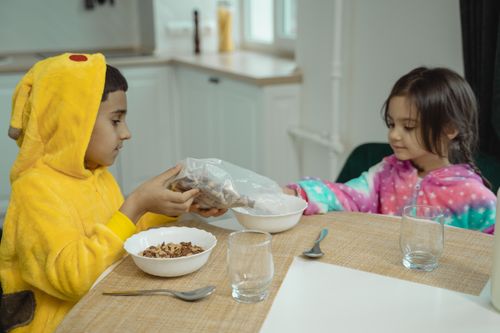 Free Children in colorful costumes sharing breakfast together at the table. Stock Photo